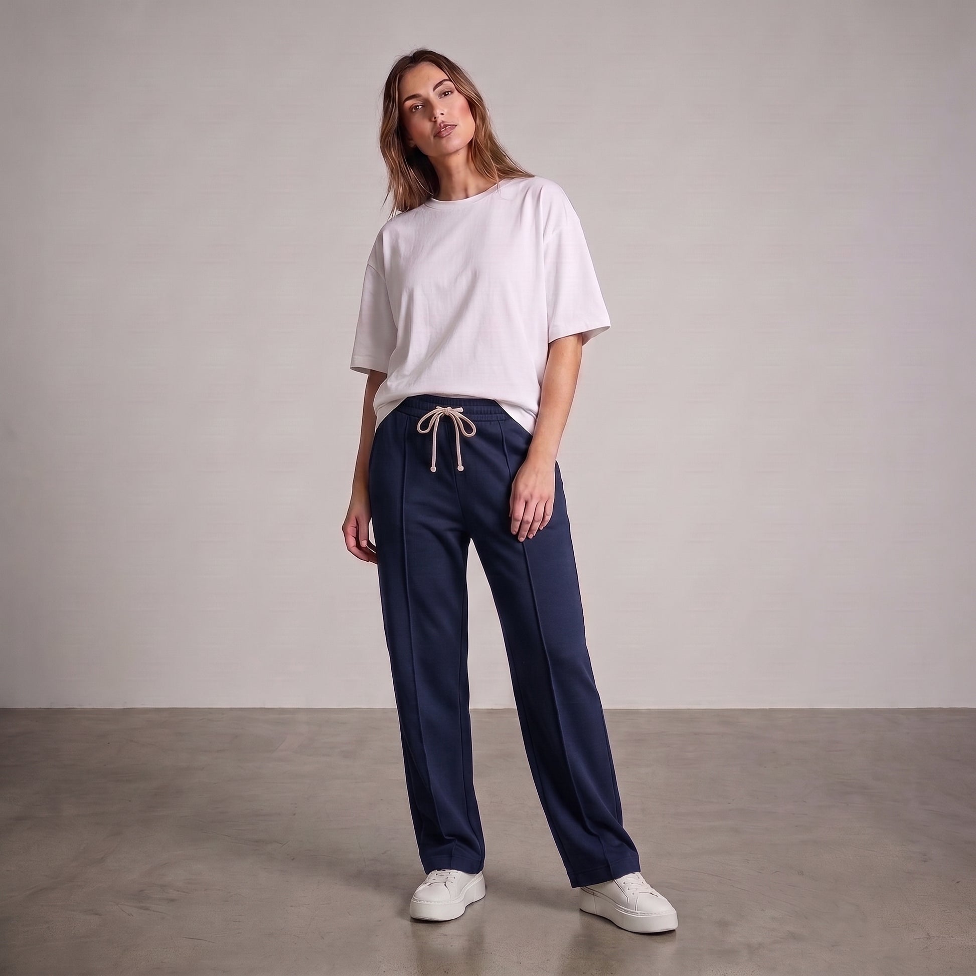 A woman modeling a pair of navy blue wide-leg baggy trouser with a beige drawstring, paired with a white t-shirt and white sneakers, standing against a neutral studio backdrop l AH Urban Wear Pk