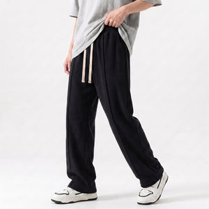 A person wearing loose black drawstring baggy trouser with a light gray t-shirt and white sneakers, shown from the waist down against a plain light background l AH Urban Wear Pk