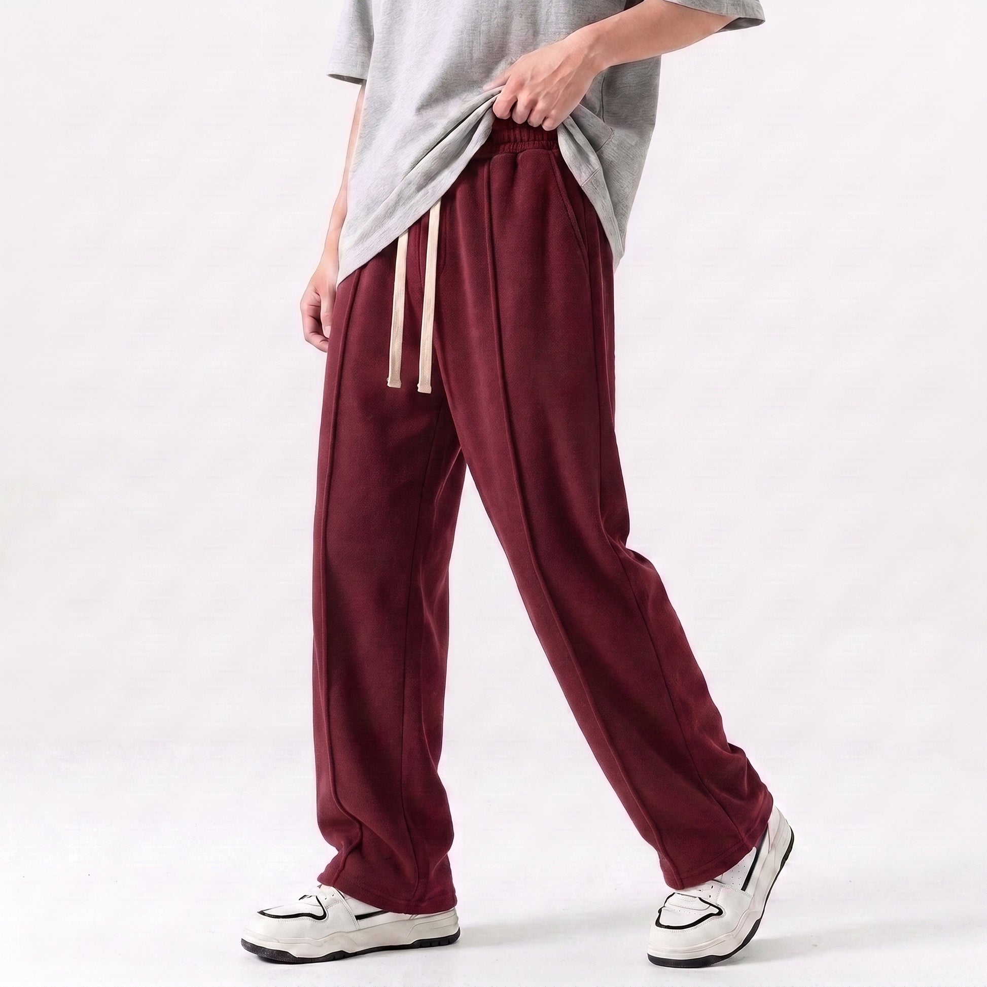 A person wearing loose maroon drawstring baggy trouser with a gray t-shirt and white sneakers, shown from the waist down against a plain light background l AH Urban Wear Pk
