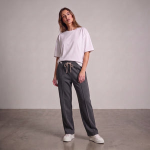 A woman modeling a light pink oversized t-shirt and dark gray drawstring baggy trouser, standing against a neutral studio backdrop l AH Urban Wear Pk