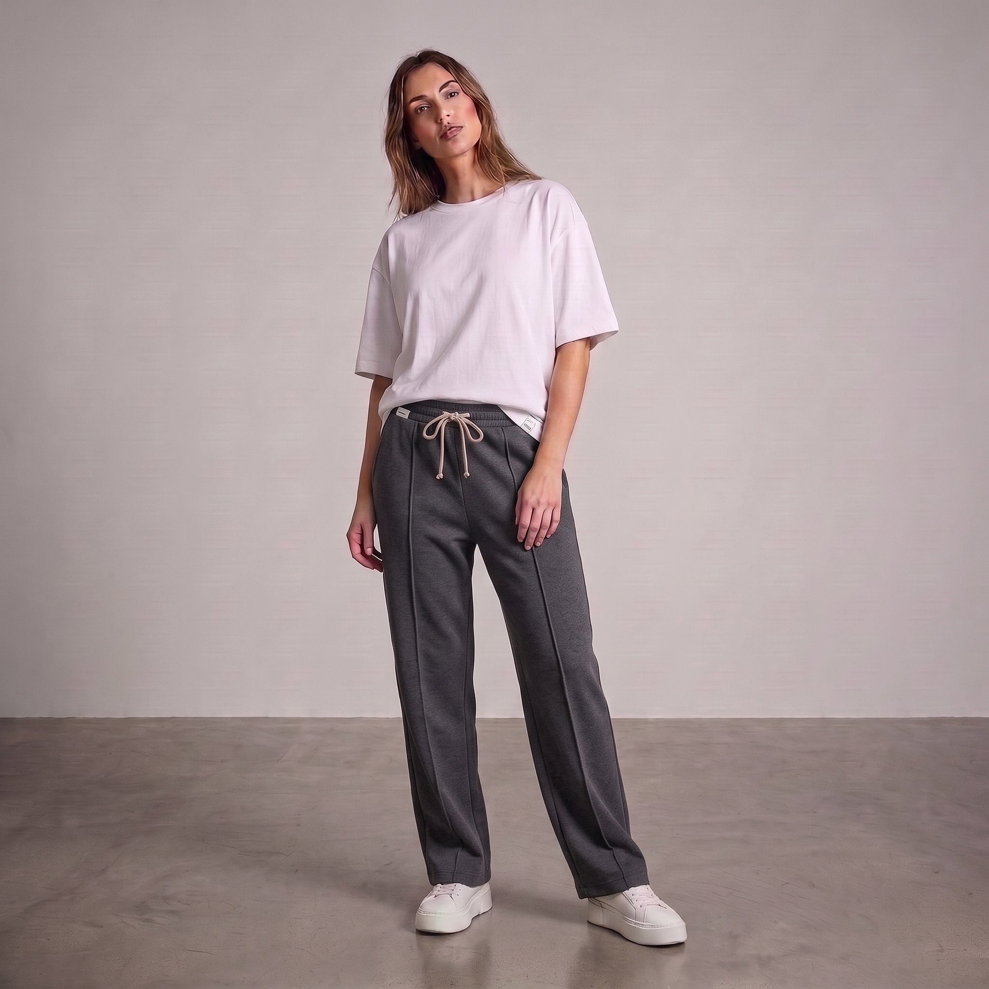 A woman modeling a light pink oversized t-shirt and dark gray drawstring baggy trouser, standing against a neutral studio backdrop l AH Urban Wear Pk