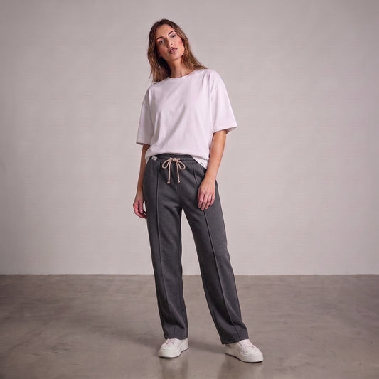 A woman modeling a light pink oversized t-shirt and dark gray drawstring baggy trouser, standing against a neutral studio backdrop l AH Urban Wear Pk