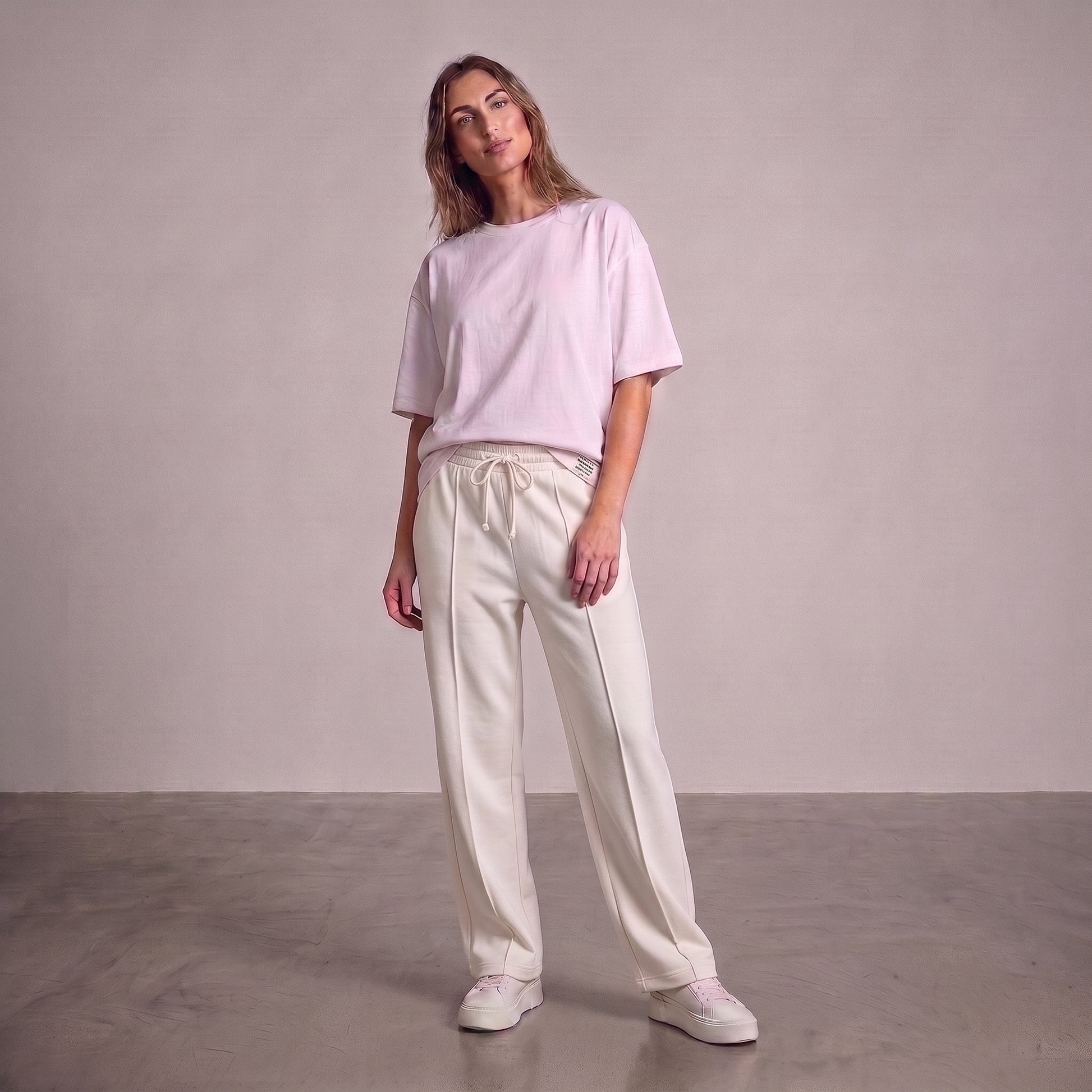 A woman modeling a light pink short-sleeve crewneck t-shirt and off-white drawstring baggy trouser against a neutral studio backdrop l AH Urban Wear Pk